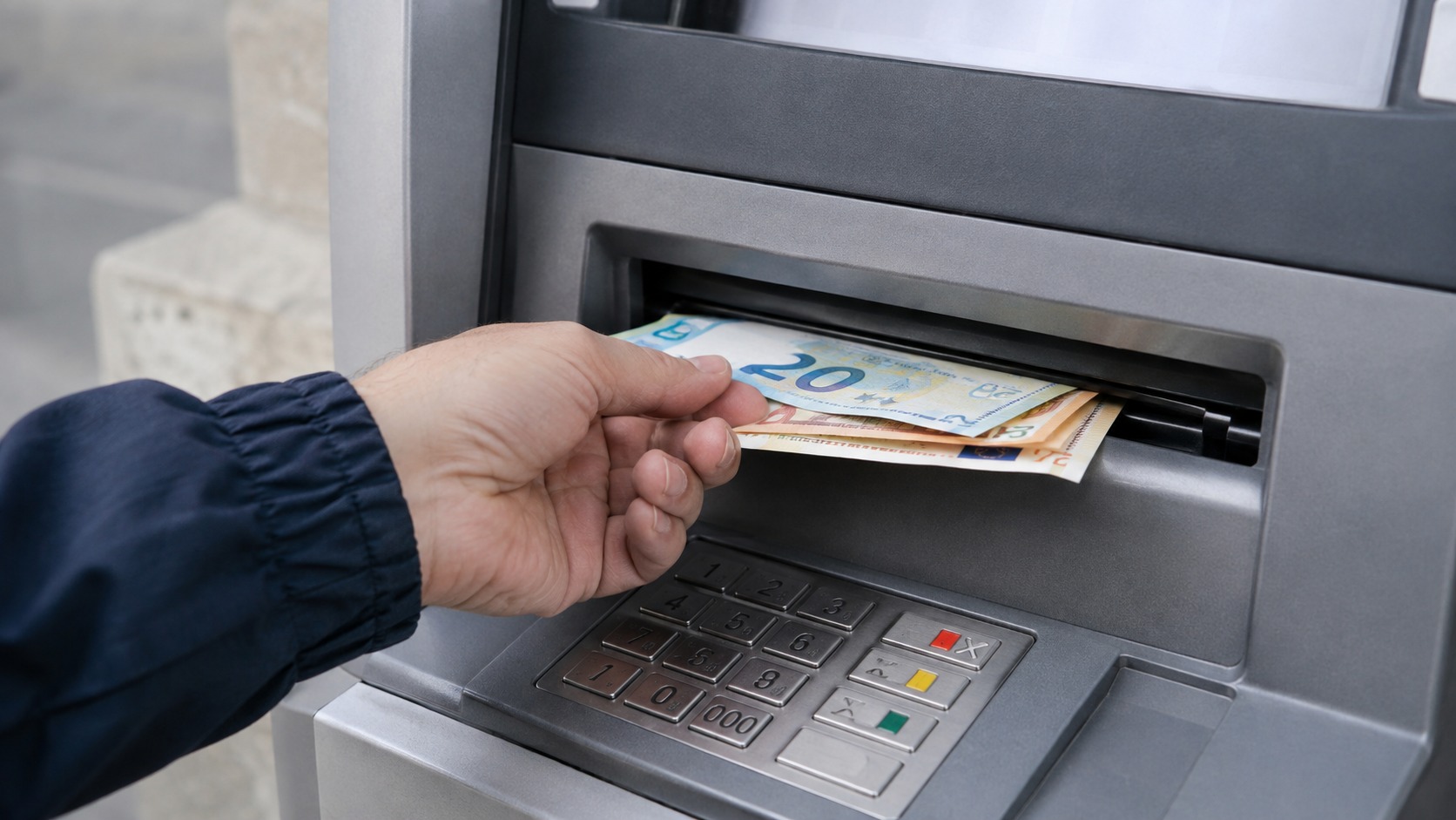 Mano che ritira banconote da uno sportello automatico